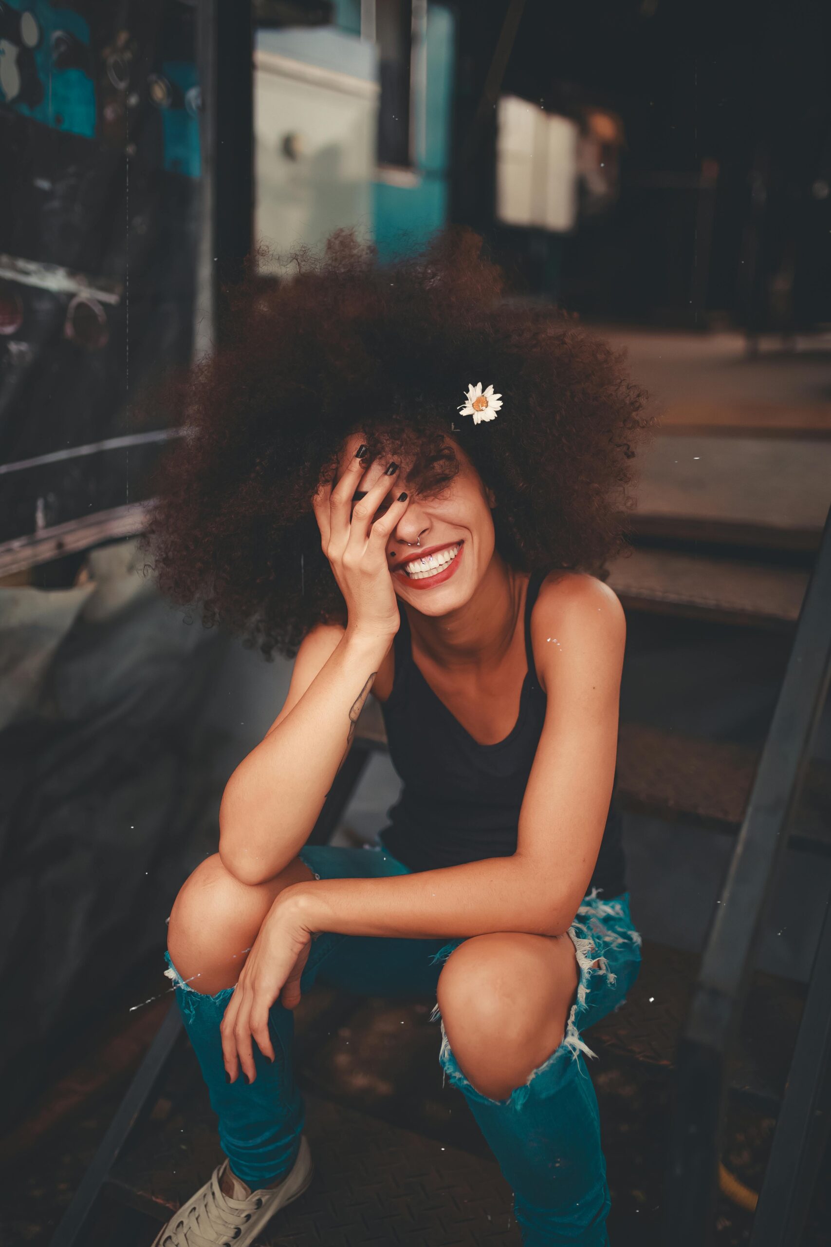Home Cheerful woman wearing ripped jeans and curly hair with flower, enjoying a sunny day outdoors.